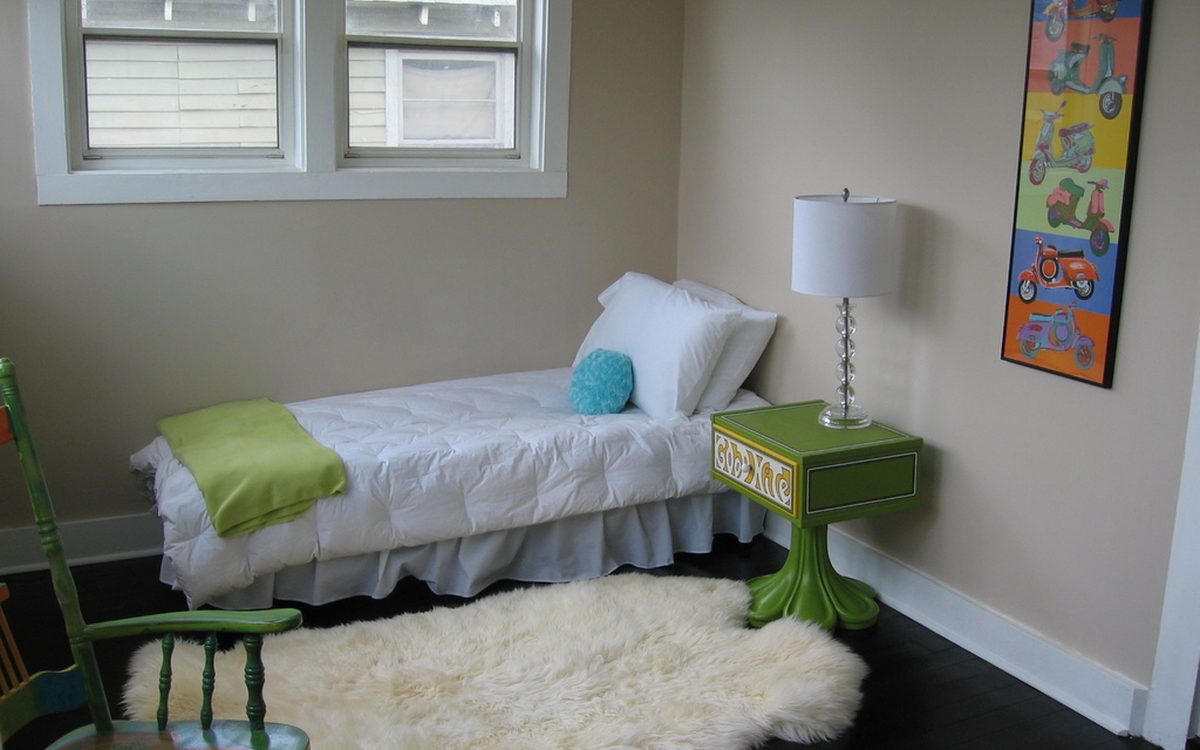 Bright bedroom with crisp white bedding, a sheepskin rug and a green bedside table