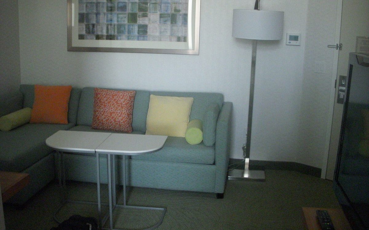 Living room with a sage green sofa, orange and yellow cushions and a white floor lamp