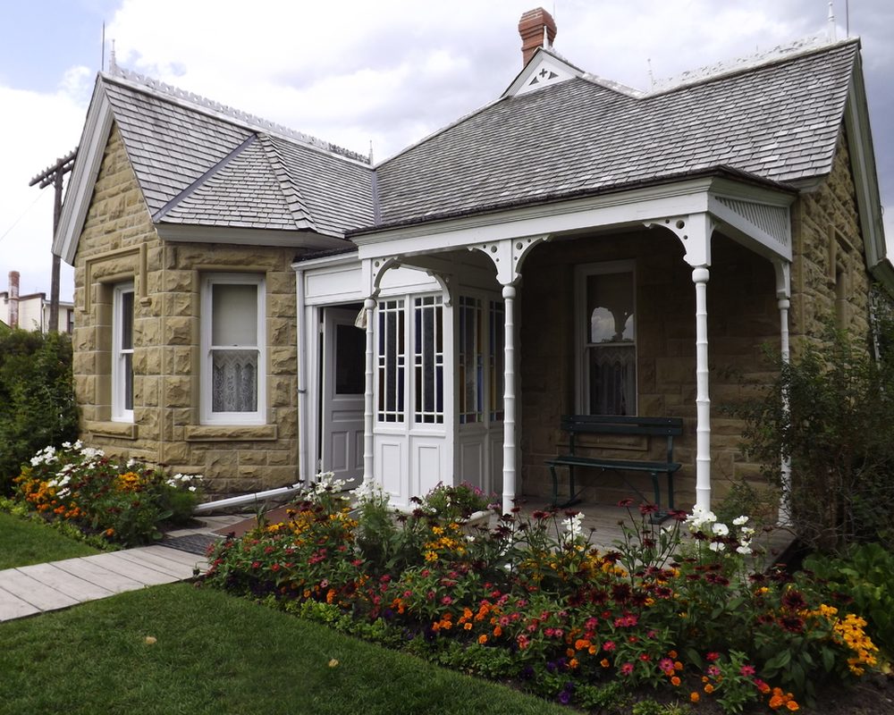 Stone cottage with a white porch and colourful flower beds