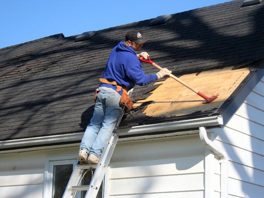 Roofer on a ladder stripping old shingles from a house roof